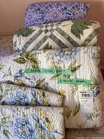 Three queen size quilts stacked, two pillow shams on top, close-up showing different quilt patterns and colors with label Large (Queen) Quilts 2 Pillow Shams