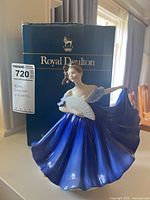 Photo of the Royal Doulton Elaine figurine standing in front of its original box. The figurine shows a woman in a flowing blue dress with white fan, fine detailing and glossy finish.