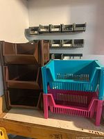 Stacked large brown, turquoise, and pink plastic bins on countertop with beige wall and shelving above