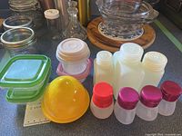 Multiple glass and plastic storage containers, small plastic bottles, and yellow plastic citrus juicer on countertop