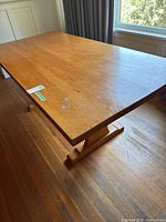 Full view of the rectangular wooden dining room table placed near a window, showing the tabletop and base structure.
