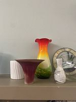 Photo of four vases including tall multicolored ruffled glass vase; white textured pottery vase; wide funnel-shaped red pottery vase; small white pottery vase with markings, and part of stained glass duck decoration.