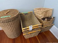 Photo of the full lot showing the round wicker hamper with lid and six different wicker baskets of various shapes and sizes stacked and arranged on the floor.