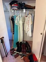 Photo showing five women's clothing items hanging in a small closet, including dresses and tops in various colors and styles, with footwear and bags arranged below the clothes