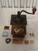 Front view of the antique coffee grinder on display with several vintage cloth patches placed around it.