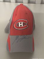Front view of red and gray Montreal Canadiens baseball cap with team logo on front and signature on brim.