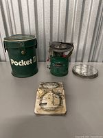Photo showing Coleman Pocket II carrying case, stove, metal lid, and instruction manual arranged on table