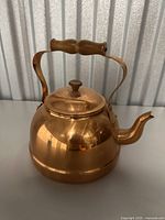 Copper kettle front side showing curved spout, wooden handle, and lid with knob.