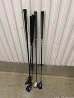Six golf clubs leaning against a wall, showing grips and shafts.