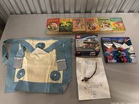 Six vintage comic books alongside two boxed LEGO sets, Staedtler colored pencils, a blue and white canvas bag with decorative round patches, and a beaded necklace on a display card.