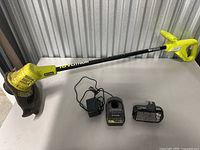 Ryobi grass trimmer with battery and charger laid out on a table.