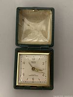 Vintage selfix wind-up travel clock housed in a green case with satin interior, showing full clock face and case.