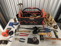 Full overview of tools on table including hammer, tape measure, pouch, pliers, saw, gloves, safety glasses, and other hand tools.