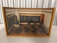 Full view of vintage miniature classroom model inside glass wooden display case showing desks, chairs, chalkboards, and classroom setup.