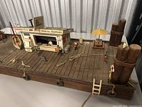 Wide view of vintage wooden harbor model display showing dock, boat, food stand, ropes, ladder, and various small figures including people and birds.