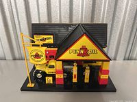 Vintage Pennzoil gas station model with two gas pumps, a truck, and a Pennzoil sign on a black base