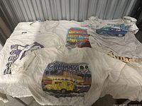 Six vintage t-shirts with various classic car and travel themed graphics laid out flat.
