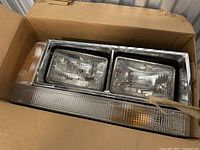 Photo of a vintage Volvo headlight assembly with chrome frame, dual rectangular lenses, clear turn signal lens, and amber side marker lens inside a cardboard box.