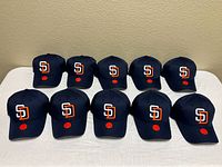 Ten identical navy San Diego Padres caps arranged on table