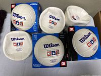 Six Wilson USYVL volleyballs on table, three in boxes three loose