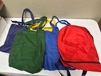 Group shot of red backpack and four colored tote bags