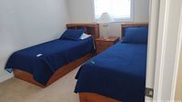 Two twin beds shown with blue bedspreads, pillows and headboards