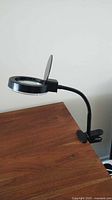 Side view of black clamp-on magnifying lamp attached to desk