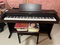 Front view of Roland HP-2-MH digital piano with bench and books on shelf