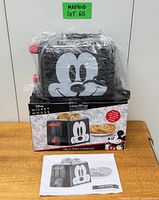 Toaster wrapped in plastic on top of its box with manual visible