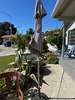 Folded beige patio umbrella mounted in stand outdoors