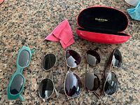 Five pairs sunglasses, Elizabeth Arden case, cleaning cloth on countertop