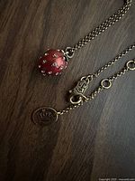 Close-up of red enamel strawberry pendant with rhinestones and chain clasp showing crown tag and Juicy Couture mark