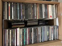 Top view of filled cardboard box showing rows of CD jewel cases with visible spine titles
