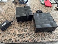 Two Nighthawk cube routers with one power adapter visible