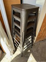 Stack of five backless metal-frame stools with dark wood seats