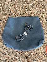 Front view of slate blue leather shoulder bag with detachable strap coiled on top