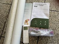 Rolled blind, remote, hardware bag, installation guide on tiled floor