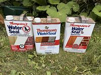 Front view of three 3.7 L Thompson's WaterSeal cans standing on grass