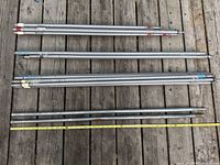 Group view of all twenty poles laid out on wooden deck with tape measure for scale