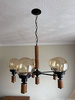 Overall view of chandelier showing five smoked glass globes, black metal frame, wood accents, ceiling canopy and chain