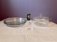 Three pie dishes stacked next to oval casserole with lid and soda can for scale