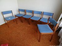 All six teak dining chairs aligned against wall