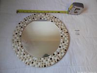 Front view of round mirror showing mosaic tile border and reflective surface with tape measure for scale