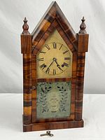 Front view of antique Atkins cathedral style wall clock with winding key placed in front showing wood finish and glass panel etched design.