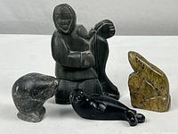 Group view of four carved stone figures including indigenous human figure and three animals on white background