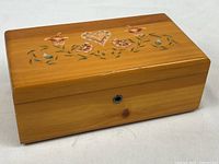 Front angled view of rectangular wooden keepsake box showing the hand painted floral and heart design on the lid and a keyhole lock on front side.