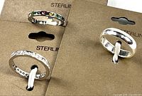 Three sterling silver rings in original brown packaging. One ring has multicolor gemstones, one has hammered texture, one is plain shiny band. All size 7.