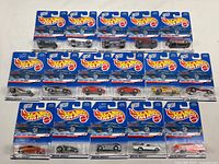 Overview of all 16 Hot Wheels 2000 First Editions die cast cars in original sealed packaging laid out in rows, showing front labels and cars through clear plastic blister packs.