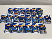 Twenty Mattel Hot Wheels die cast cars arranged flat on a white surface, all in sealed original packaging with blue backing cards.