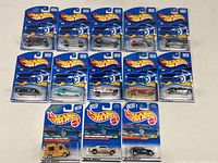 Lot of 13 Mattel Hot Wheels die cast cars in original sealed blue packaging laid out in rows showing front of packages with clear plastic bubbles.